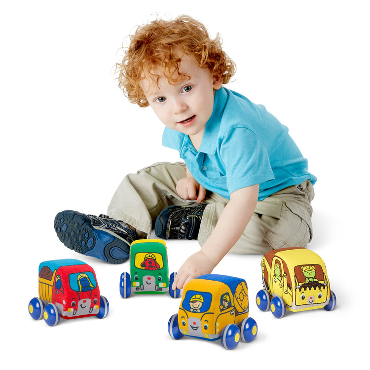 A child on white background with The Melissa & Doug Pull-Back Construction Vehicles - Soft Baby Toy Play Set of 4 Vehicles