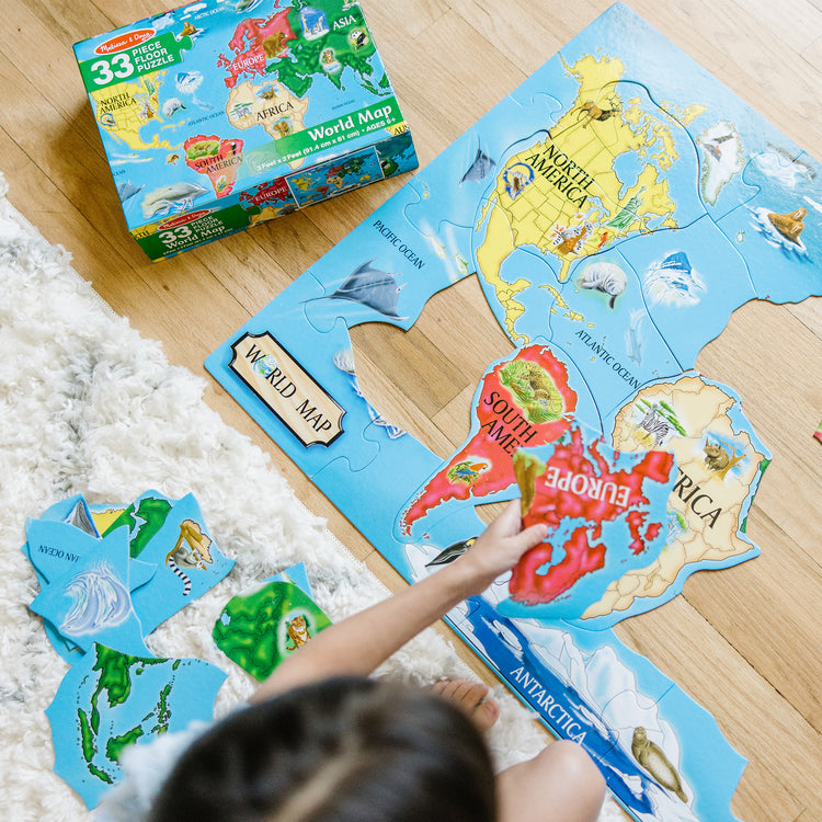 A kid playing with The Melissa & Doug World Map Jumbo Jigsaw Floor Puzzle (33 pcs, 2 x 3 feet)