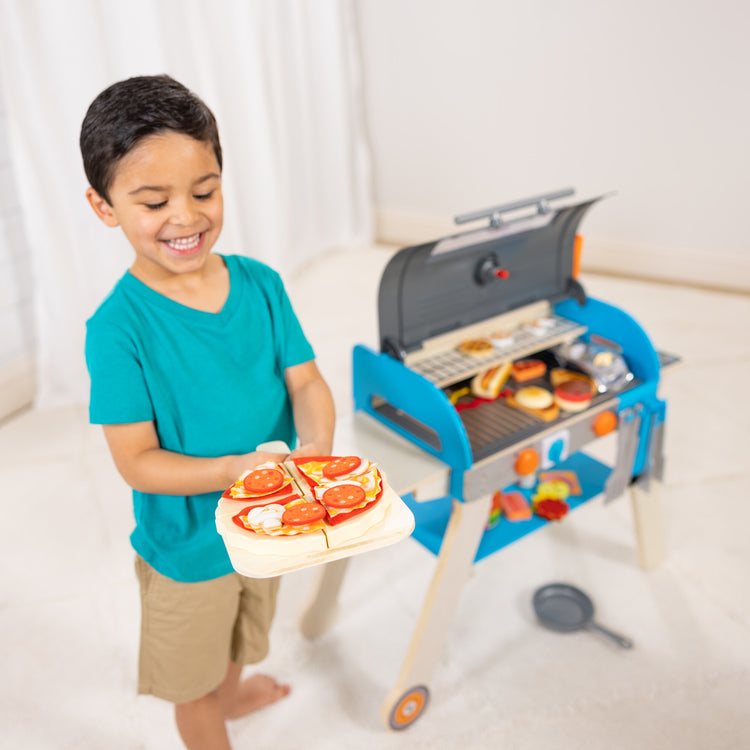 A kid playing with The Melissa & Doug Wooden Deluxe Barbecue Grill, Smoker and Pizza Oven Play Food Toy for Pretend Play Cooking for Kids