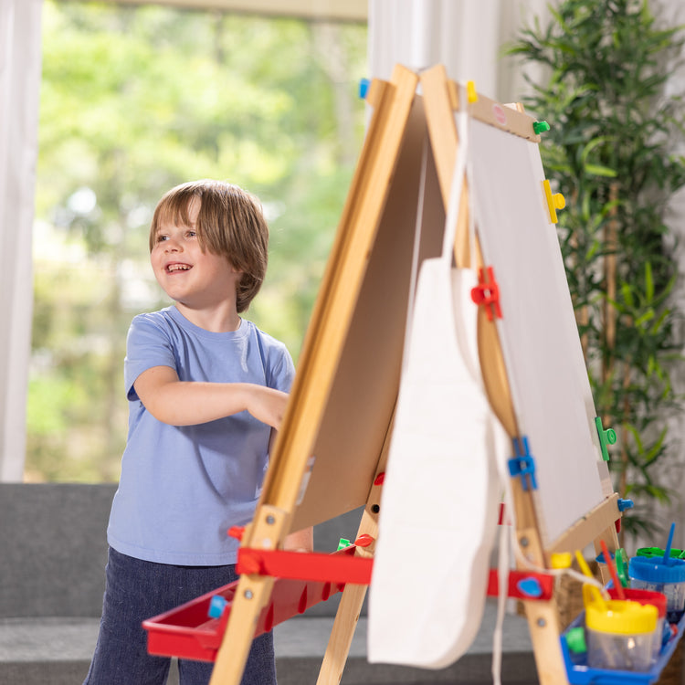 A kid playing with The Melissa & Doug Deluxe Standing Art Easel - Dry-Erase Board, Chalkboard, Paper Roller