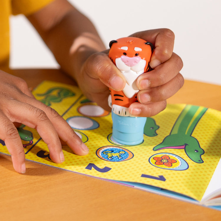 A kid playing with The Melissa & Doug Sticker WOW!™ Tiger Bundle: Sticker Stamper, 24-Page Activity Pad, 600 Total Stickers, Arts and Crafts Fidget Toy Collectible Character
