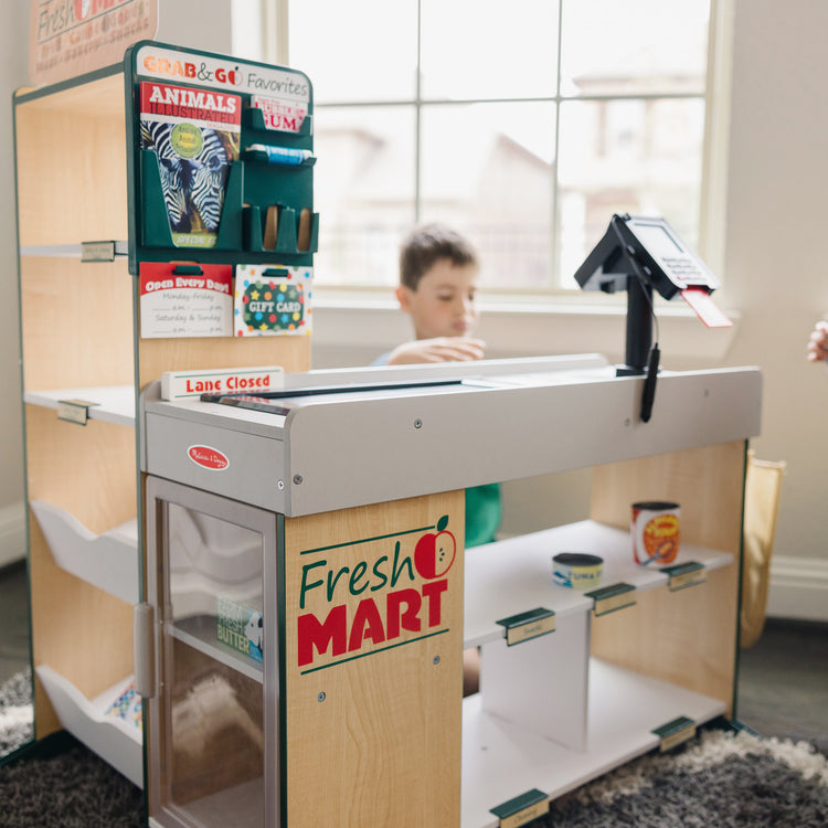 A kid playing with The Melissa & Doug Freestanding Wooden Fresh Mart Grocery Store