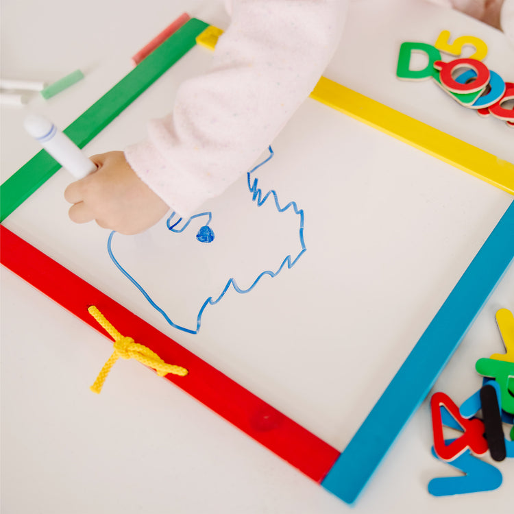 A kid playing with The Melissa & Doug Magnetic Chalkboard and Dry-Erase Board With 36 Magnets (Numbers and Uppercase Letters), Chalk, Eraser, and Dry-Erase Pen
