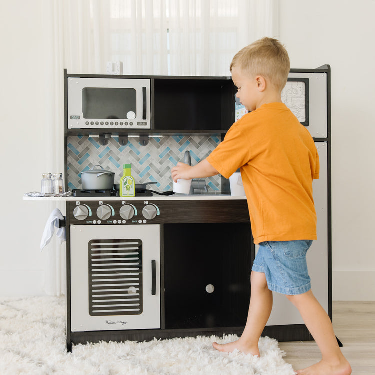 A kid playing with The Melissa & Doug Chef's Wooden Pretend Play Kitchen for Kids With “Ice” Cube Dispenser – Charcoal Gray