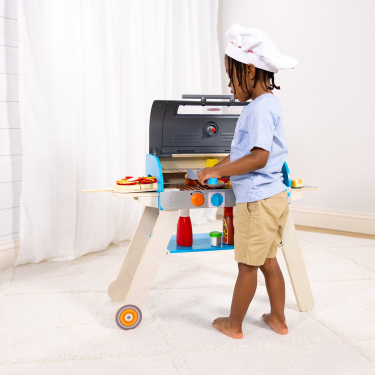 A kid playing with The Melissa & Doug Wooden Deluxe Barbecue Grill, Smoker and Pizza Oven Play Food Toy for Pretend Play Cooking for Kids