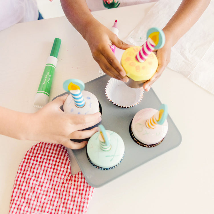 A kid playing with The Melissa & Doug Bake and Decorate Wooden Cupcake Play Food Set