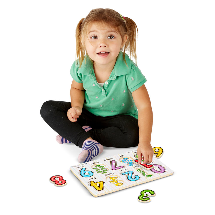 A child on white background with The Melissa & Doug Lift & See Numbers Wooden Peg Puzzle - 10 Pieces