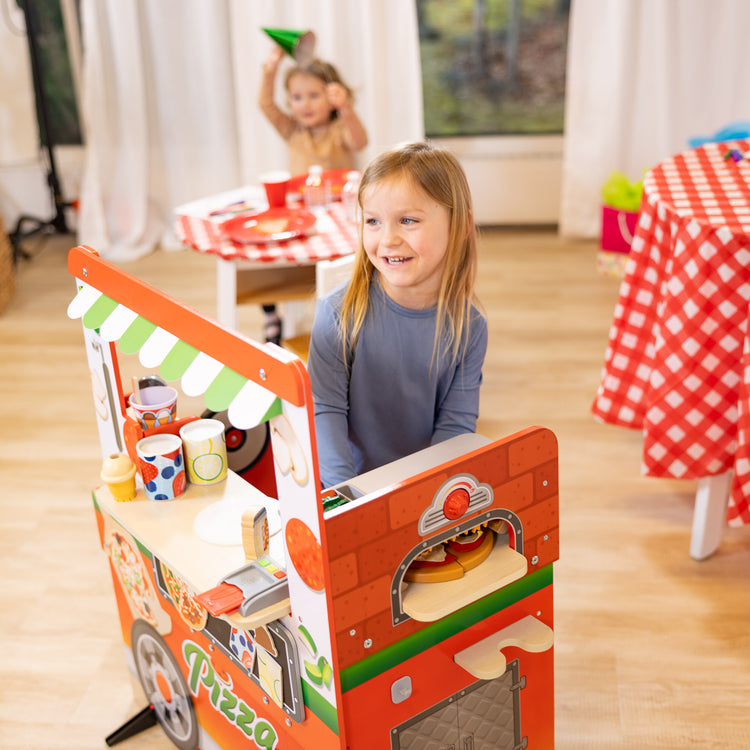A kid playing with The Melissa & Doug Wooden Pizza Food Truck Activity Center with Play Food, for Boys and Girls 3+