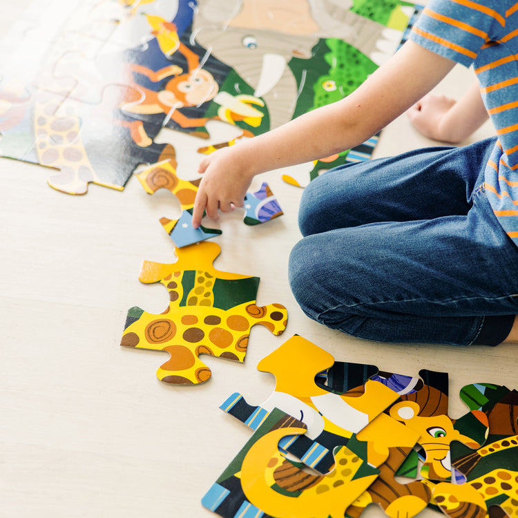 A kid playing with The Melissa & Doug Safari Social Jumbo Jigsaw Floor Puzzle (24 pcs, 2 x 3 feet)