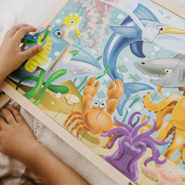 A kid playing with The Melissa & Doug Under the Sea Ocean Animals Wooden Jigsaw Puzzle With Storage Tray (24 pcs)