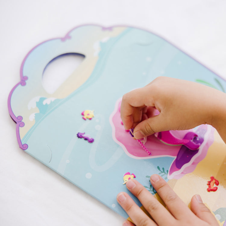 A kid playing with The Melissa & Doug Puffy Sticker Activity Book: Mermaids - 65 Reusable Stickers
