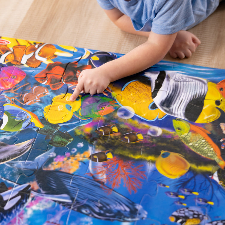 A kid playing with The Melissa & Doug Underwater Ocean Floor Puzzle (48 pcs, 2 x 3 feet)