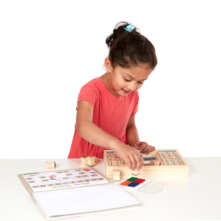 A child on white background with The Melissa & Doug Deluxe Letters and Numbers Wooden Stamp Set ABCs 123s With Activity Book, 4-Color Stamp Pad