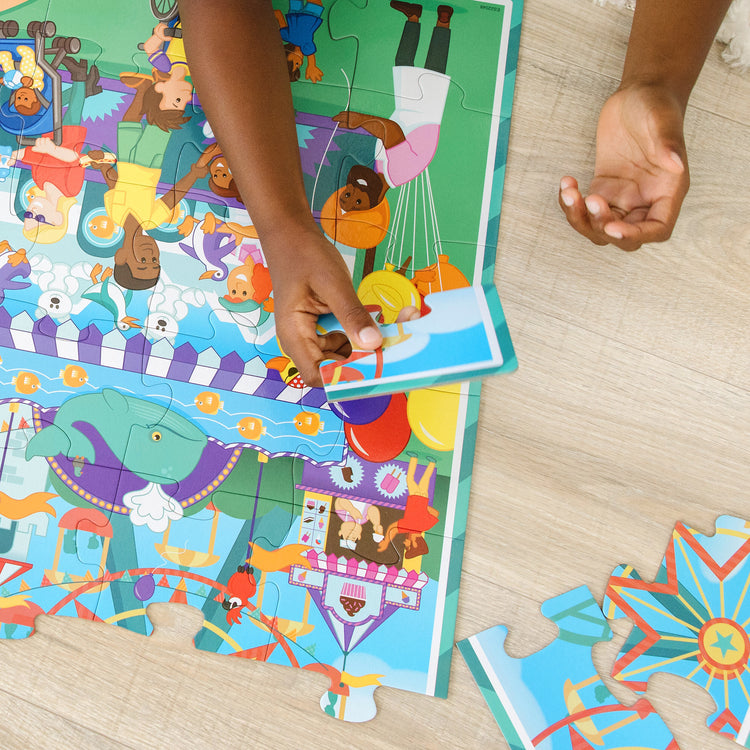 A kid playing with The Melissa & Doug Fun at the Fair! Cardboard Jigsaw Search & Find Floor Puzzle – 48 Pieces