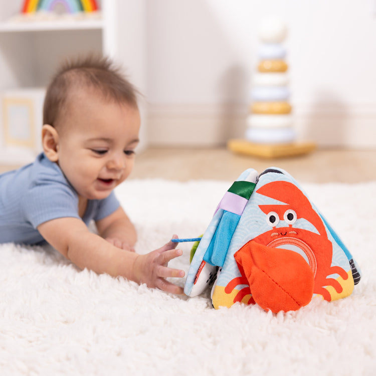 A kid playing with The Melissa & Doug Ocean Tummy Time Triangle Infant Baby Toy, Soft Sensory Toy with Textures, Mirror, Floor Toy for Newborns to Ages 6 Months