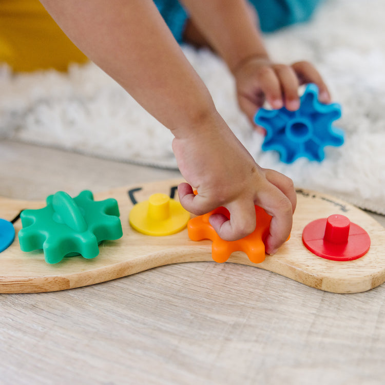 A kid playing with The Melissa & Doug Wooden Rainbow Caterpillar Gears Toddler Toy With 6 Interchangeable Gears