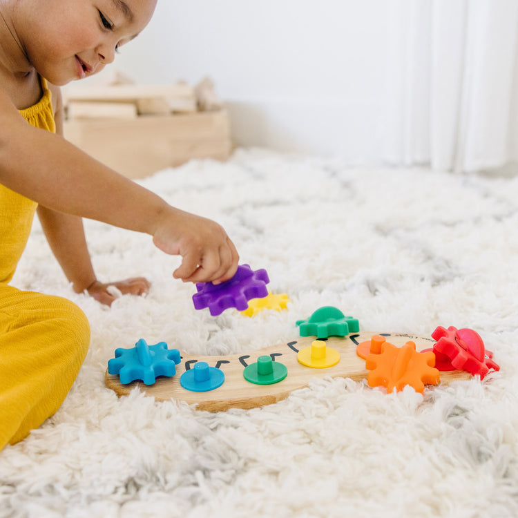 A kid playing with The Melissa & Doug Wooden Rainbow Caterpillar Gears Toddler Toy With 6 Interchangeable Gears