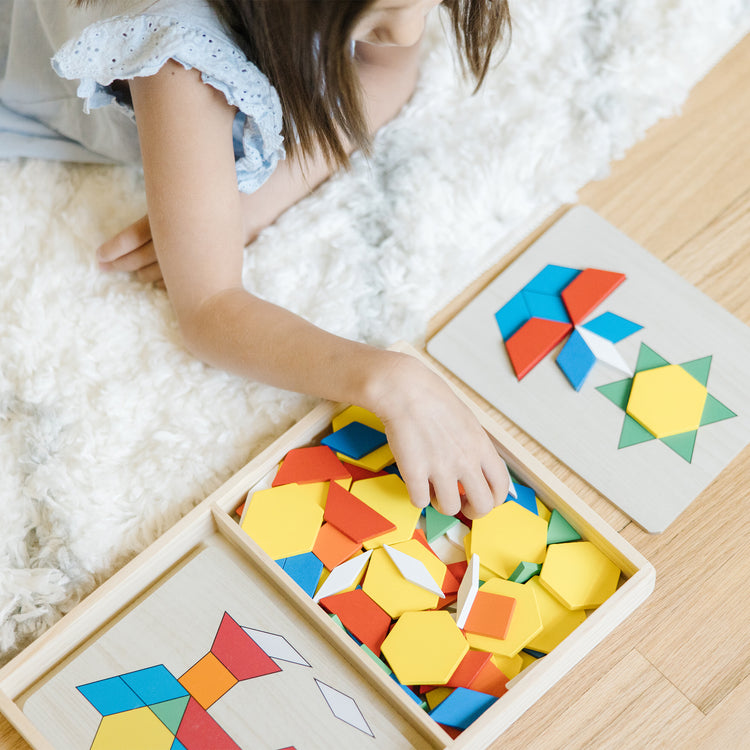 A kid playing with The Melissa & Doug Pattern Blocks and Boards - Classic Toy With 120 Solid Wood Shapes and 5 Double-Sided Panels, Multi-Colored Animals Puzzle