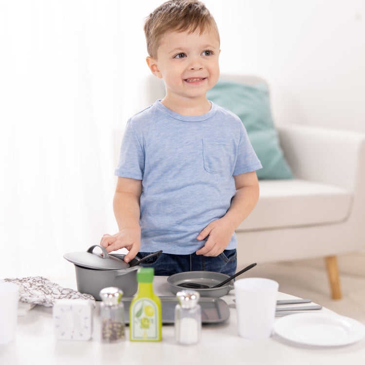 A kid playing with The Melissa & Doug 22-Piece Play Kitchen Accessories Set - Utensils, Pot, Pans, and More
