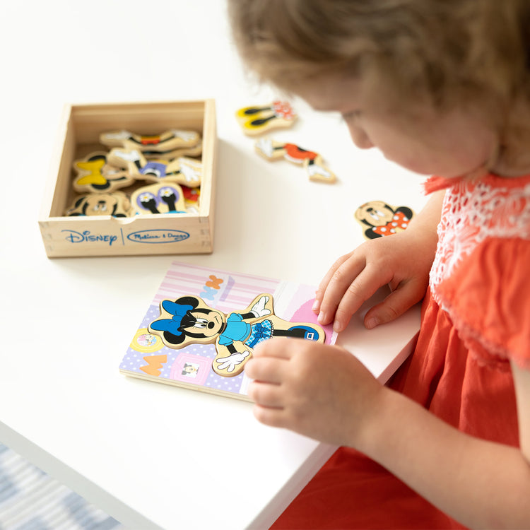 A kid playing with The Melissa & Doug Disney Minnie Mouse Mix and Match Dress-Up Wooden Play Set Puzzle (18 pcs)
