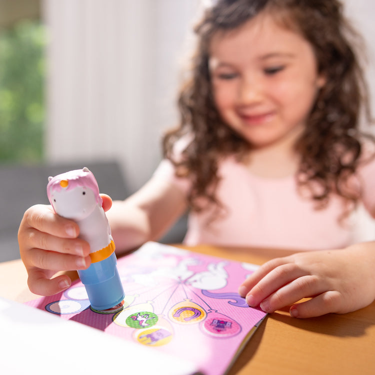 A kid playing with The Melissa & Doug Sticker WOW!™ Unicorn Bundle: Sticker Stamper, 24-Page Activity Pad, 600 Total Stickers, Arts and Crafts Fidget Toy Collectible Character