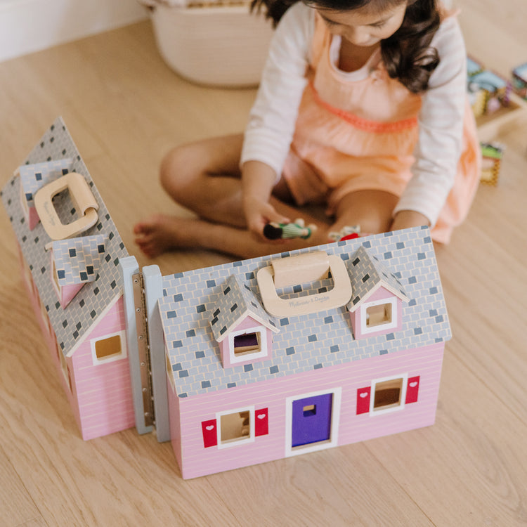 A kid playing with The Melissa & Doug Fold and Go Wooden Dollhouse With 2 Dolls and Wooden Furniture