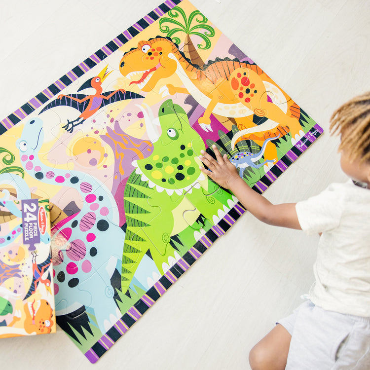 A kid playing with The Melissa & Doug Dinosaur Dawn Jumbo Jigsaw Floor Puzzle (24 pcs, 2 x 3 feet)