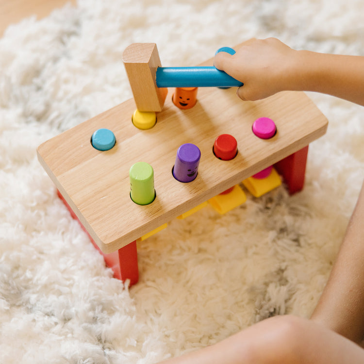 A kid playing with The Melissa & Doug Deluxe Pounding Bench Wooden Toy With Mallet
