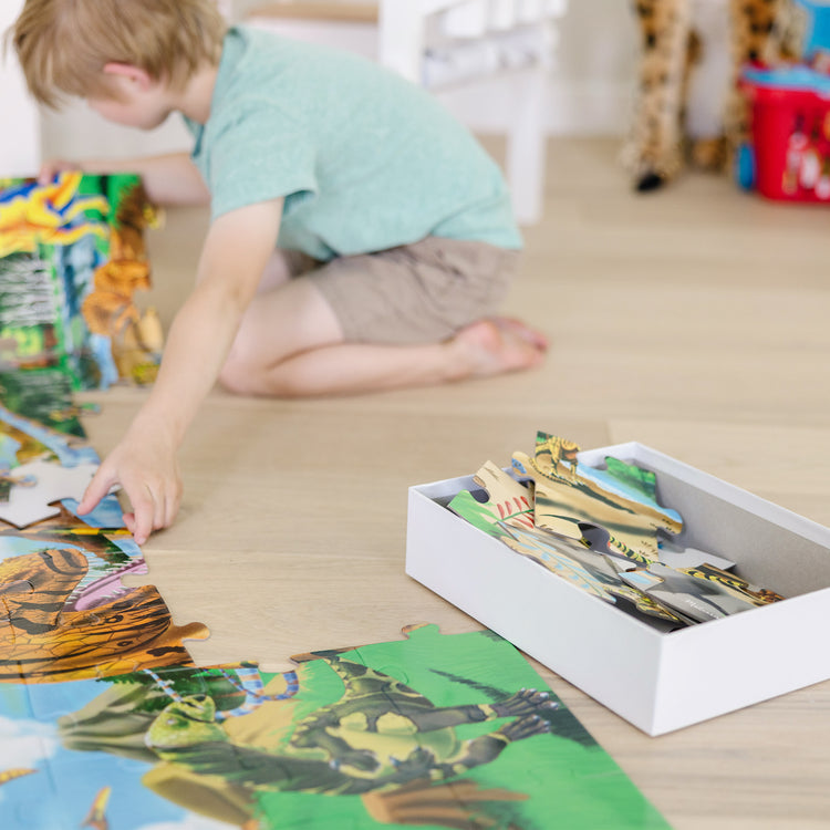 A kid playing with The Melissa & Doug Land of Dinosaurs Floor Puzzle (48 pcs, 4 feet long)