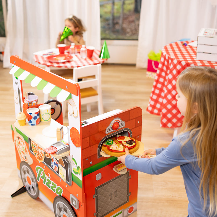 A kid playing with The Melissa & Doug Wooden Pizza Food Truck Activity Center with Play Food, for Boys and Girls 3+