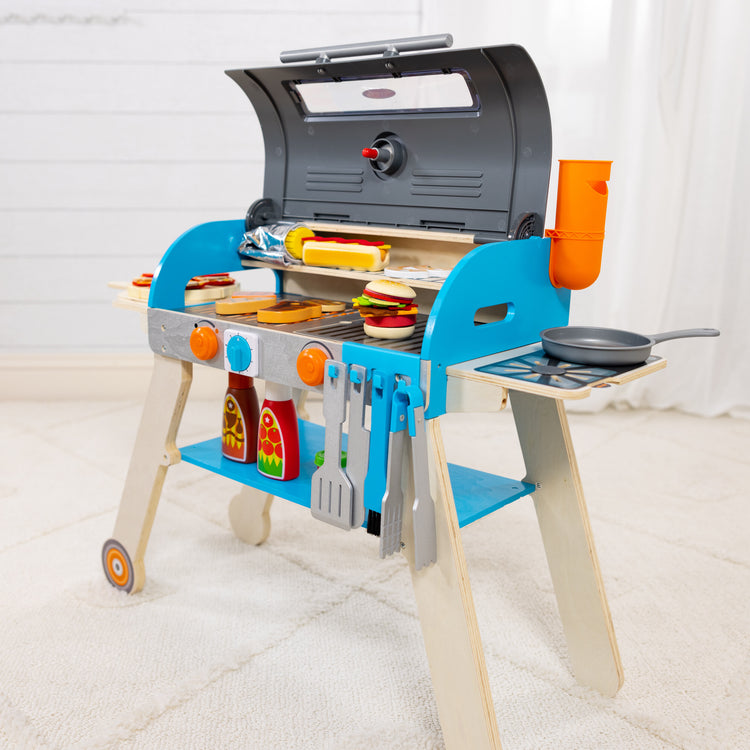 A playroom scene with The Melissa & Doug Wooden Deluxe Barbecue Grill, Smoker and Pizza Oven Play Food Toy for Pretend Play Cooking for Kids