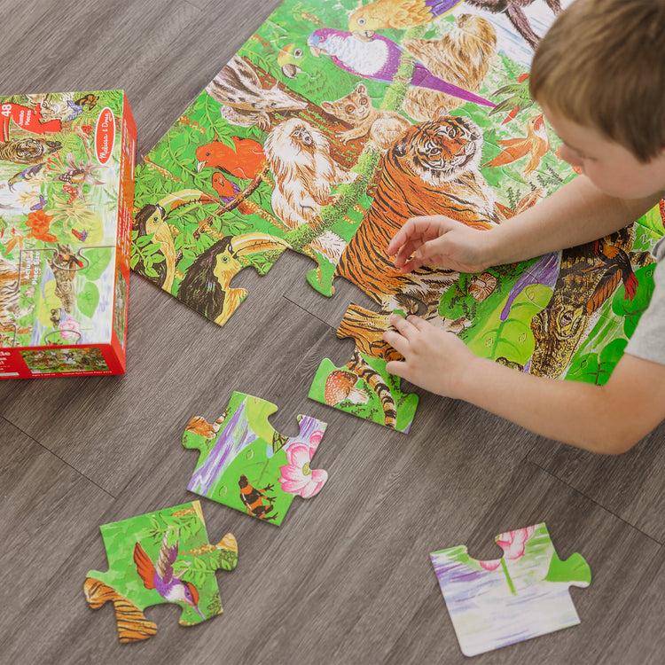 A kid playing with The Melissa & Doug Rainforest Floor Puzzle (48 pcs, 2 x 3 feet)