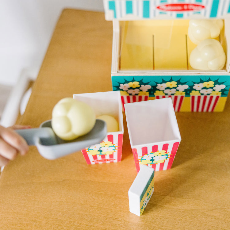 A kid playing with The Melissa & Doug Fun at the Fair! Wooden Popcorn Popping Play Food Set