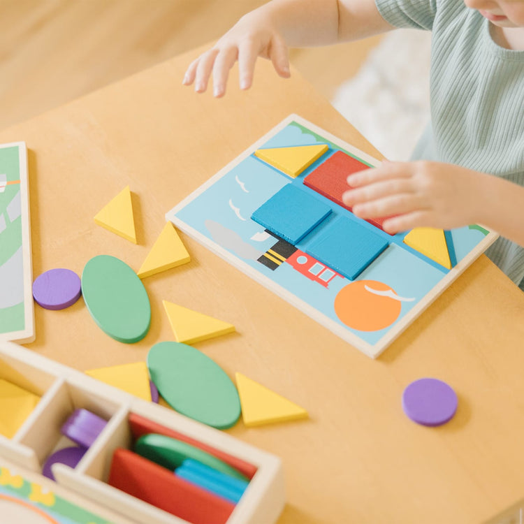 A kid playing with the Melissa & Doug Beginner Wooden Pattern Blocks Educational Toy With 5 Double-Sided Scenes and 30 Shapes