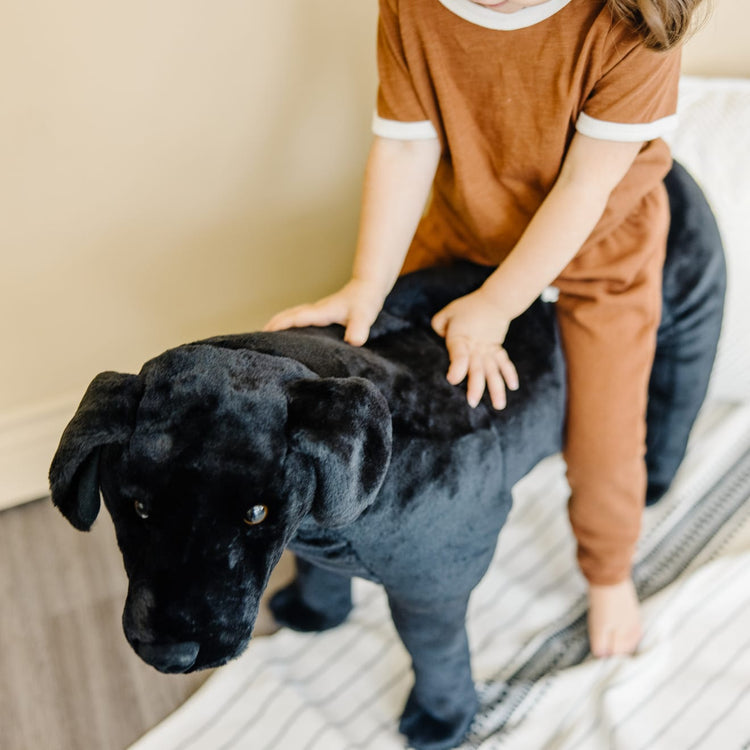 A kid playing with the Melissa & Doug Giant Black Lab - Lifelike Stuffed Animal Dog (over 2 feet tall)