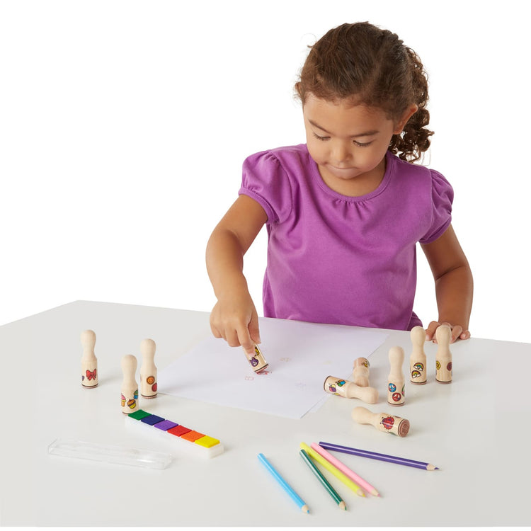 A child on white background with the Melissa & Doug Deluxe Happy Handle Stamp Set With 10 Stamps, 5 Colored Pencils, and 6-Color Washable Ink Pad