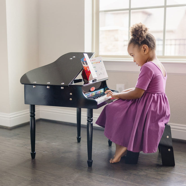 A kid playing with the Melissa & Doug Learn-To-Play Classic Grand Piano With 30 Keys, Color-Coded Songbook, and Non-Tip Bench