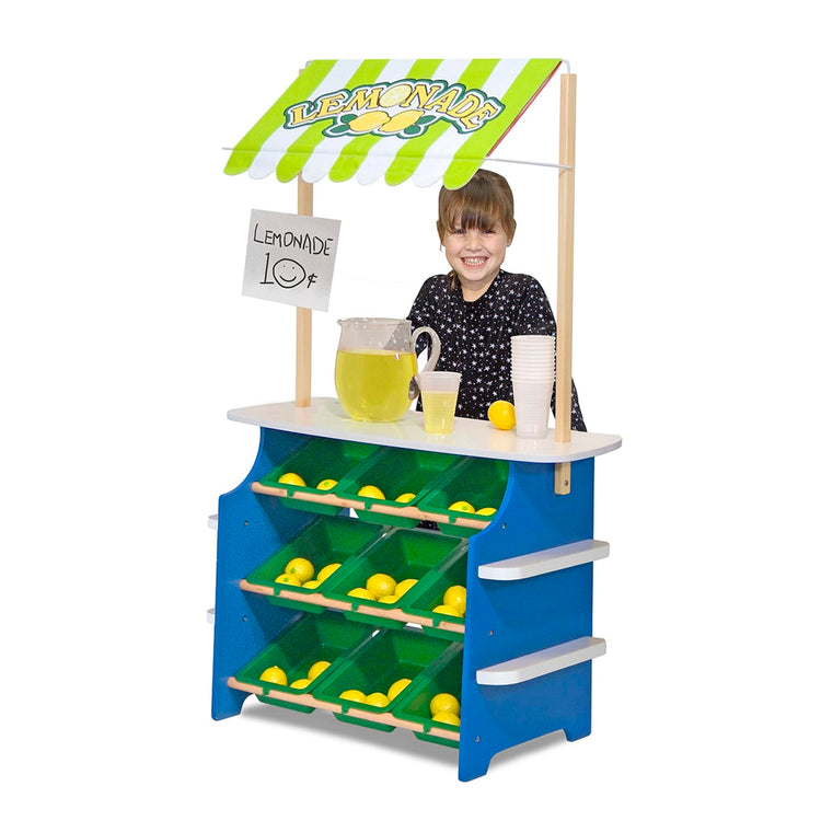 A child on white background with the Melissa & Doug Wooden Grocery Store and Lemonade Stand - Reversible Awning, 9 Bins, Chalkboards