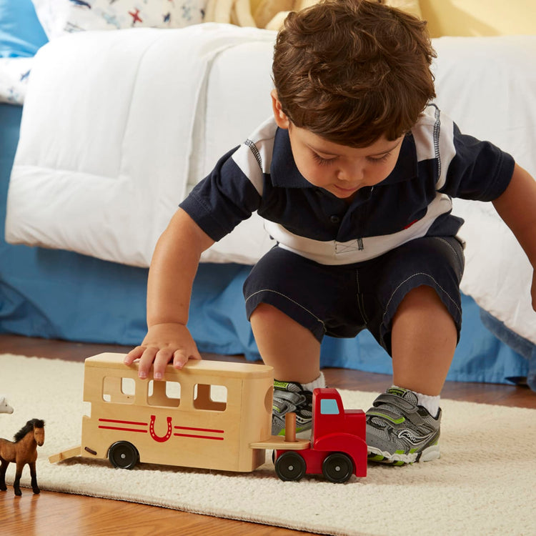 A kid playing with the Melissa & Doug Horse Carrier Wooden Vehicle Play Set With 2 Flocked Horses and Pull-Down Ramp