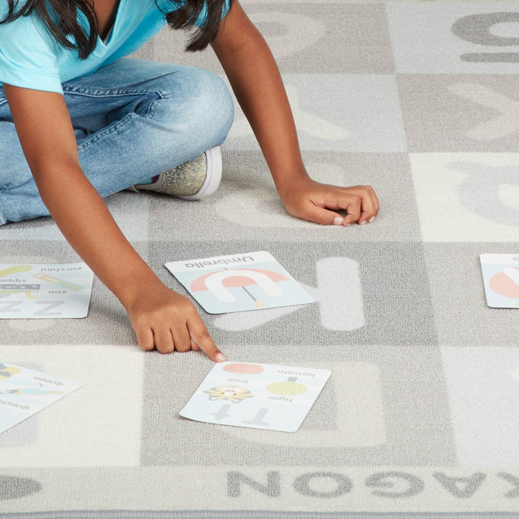A child on white background with the Melissa & Doug Jumbo ABC-123 Rug Neutral (58 x 79 inches – 36 Game Cards)