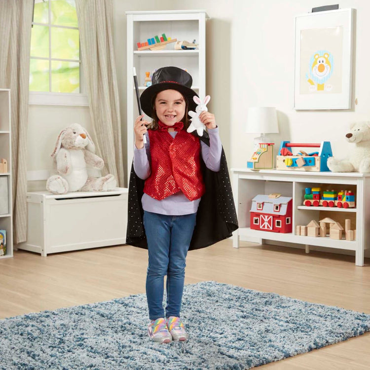 A kid playing with the Melissa & Doug Magician Costume Role Play Set - Includes Hat, Cape, Wand, Magic Tricks