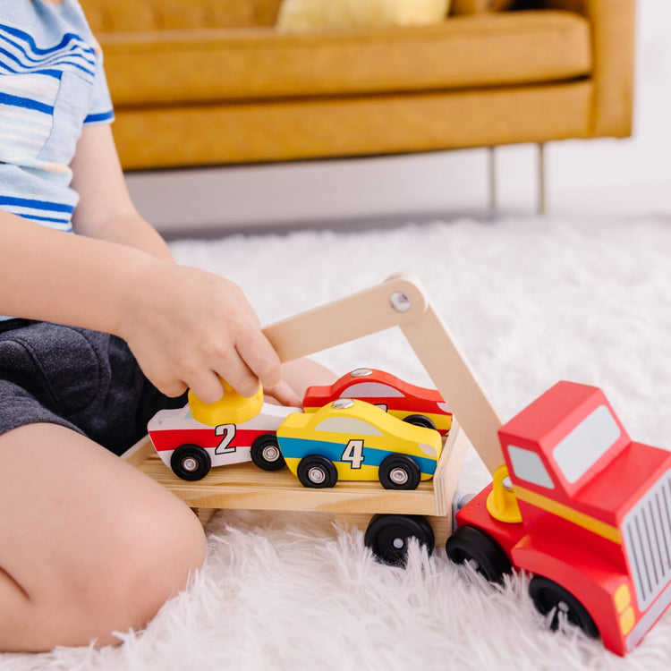 A kid playing with the Melissa & Doug Magnetic Car Loader Wooden Toy Set With 4 Cars and 1 Semi-Trailer Truck