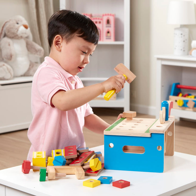 A kid playing with the Melissa & Doug Hammer and Saw Tool Bench - Wooden Building Set (32 pcs)