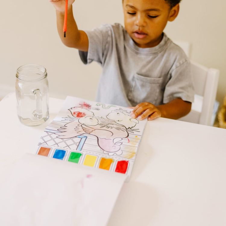 A kid playing with the Melissa & Doug Paint With Water - Farm Animals, 20 Perforated Pages, Spillproof Palettes