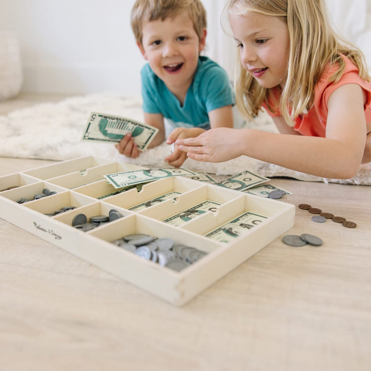 A kid playing with the Melissa & Doug Play Money Set - Educational Toy With Paper Bills and Plastic Coins (50 of Each Denomination) and Wooden Cash Drawer for Storage