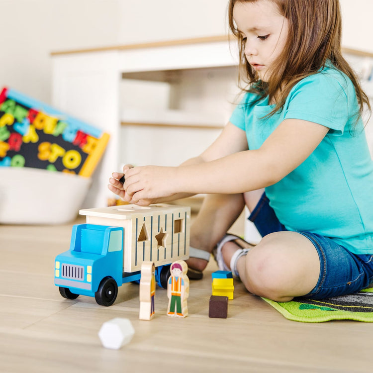 A kid playing with the Melissa & Doug Shape-Sorting Wooden Dump Truck Toy With 9 Colorful Shapes and 2 Play Figures