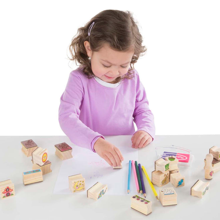 A child on white background with the Melissa & Doug Stamp-a-Scene Stamp Pad: Fairy Garden - 20 Wooden Stamps, 5 Colored Pencils, and 2-Color Stamp Pad