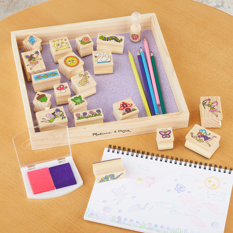 The front of the box for the Melissa & Doug Stamp-a-Scene Stamp Pad: Fairy Garden - 20 Wooden Stamps, 5 Colored Pencils, and 2-Color Stamp Pad