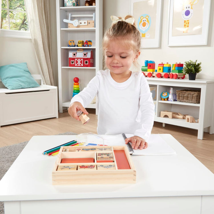A kid playing with the Melissa & Doug Wooden Stamp Set: Vehicles - 10 Stamps, 5 Colored Pencils, 2-Color Stamp Pad
