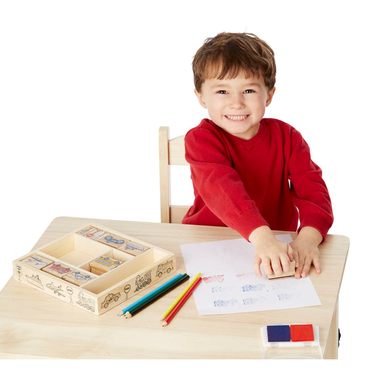 A child on white background with the Melissa & Doug Wooden Stamp Set: Vehicles - 10 Stamps, 5 Colored Pencils, 2-Color Stamp Pad